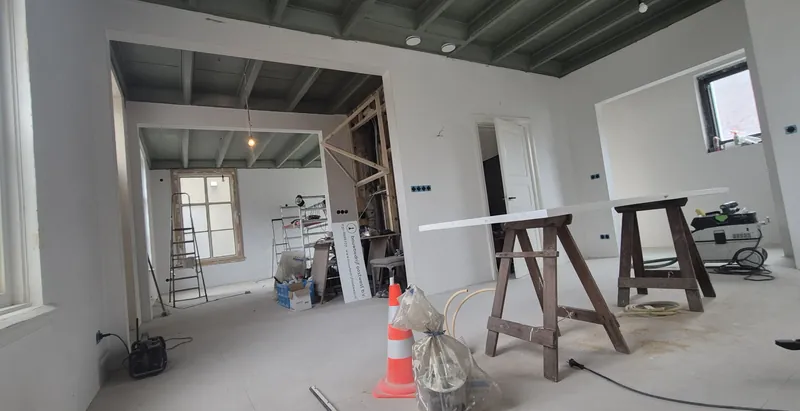 Ruime kamer in de afbouwfase met geschilderd balkenplafond, schragen, gereedschap en een pylon