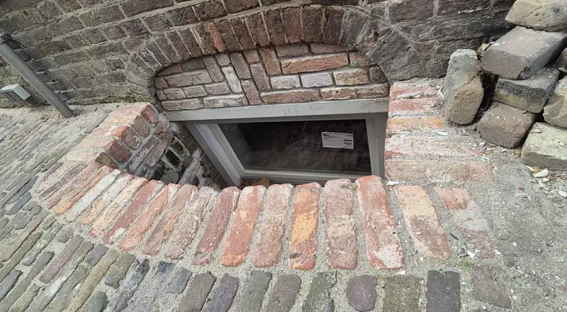 Gemetselde lichtschacht van oude bakstenen met een nieuw kelderraam, van bovenaf gezien